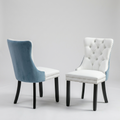 Two upholstered dining chairs shown on a light gray studio background. One chair is shown from the back in dusty blue velvet with a white seat and black legs; the other is shown from the front in white upholstery with tufted detailing, silver nailhead trim, and black legs.