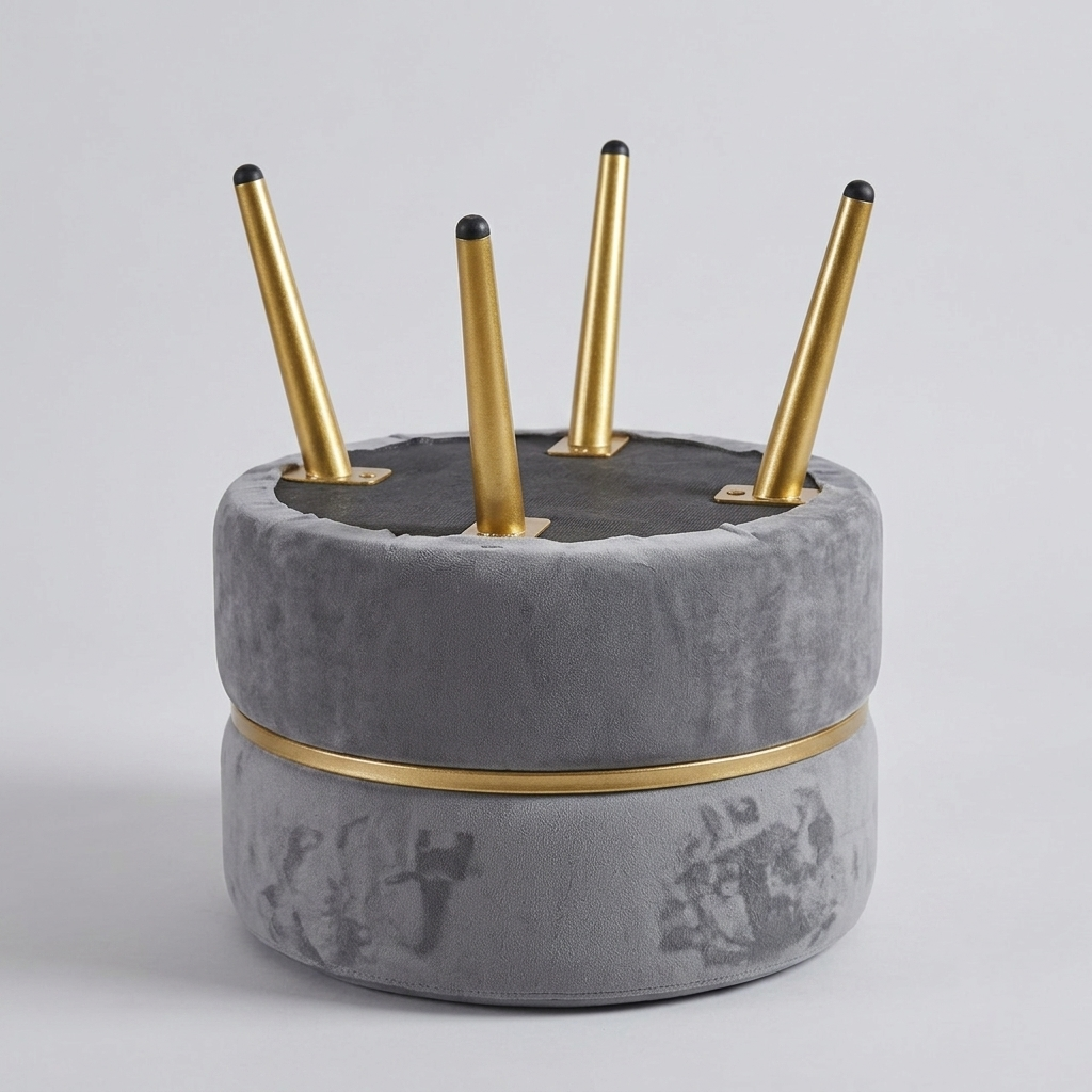 A modern round ottoman or stool in gray velvet with a gold metallic band and four gold metal legs, shown on a light gray studio background.