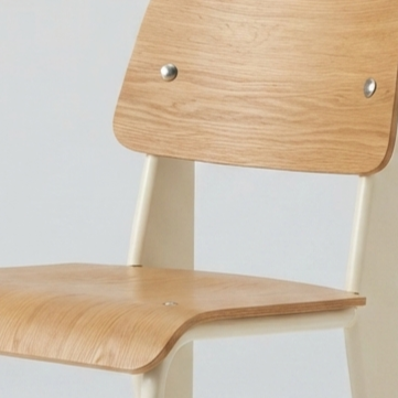 Close-up of a modern wooden chair with a light oak seat and backrest, featuring silver metal rivets and cream-colored legs against a plain light gray background.