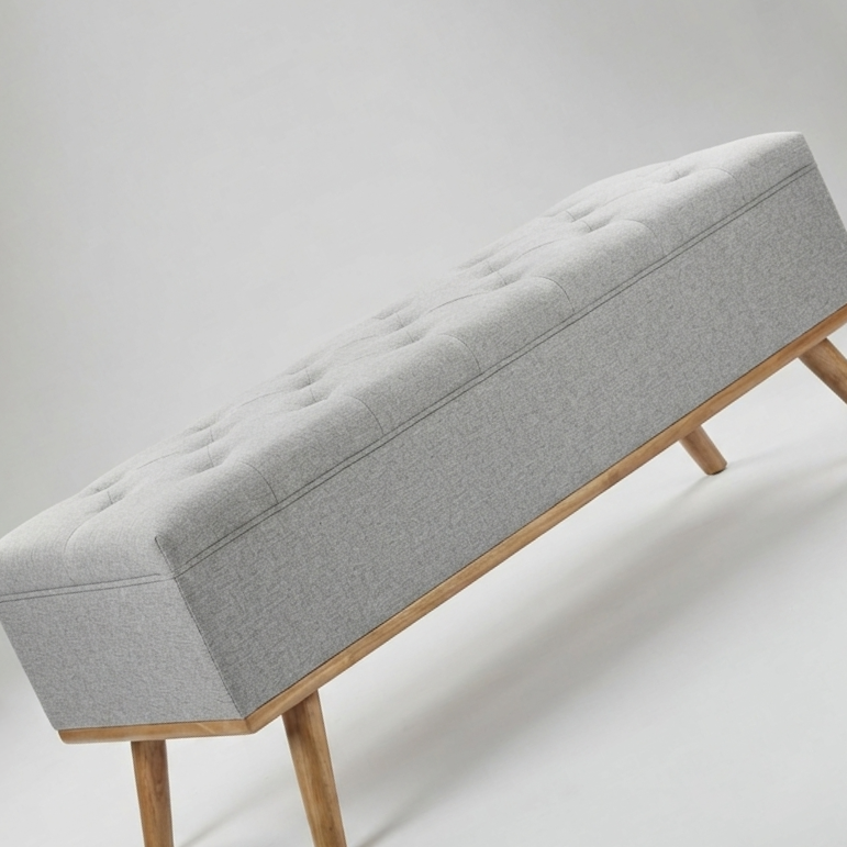 A modern upholstered bench with a light gray tufted seat cushion, natural wood frame, and tapered wooden legs, shown on a light gray studio background.