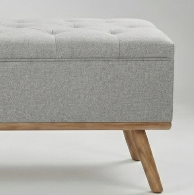 A light gray tufted storage bench with a natural wood frame and angled legs, shown against a neutral light gray background.