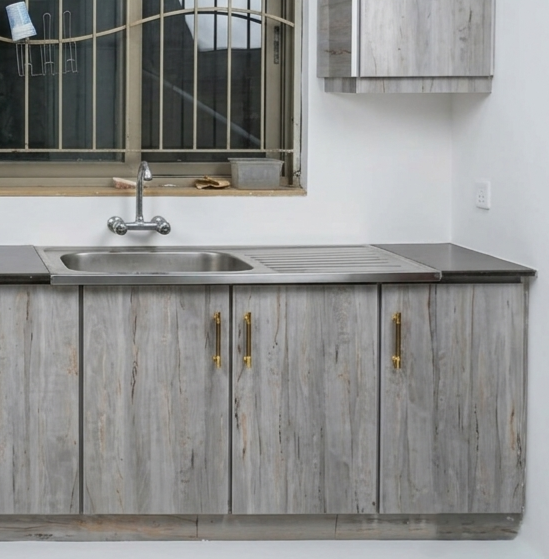Gray wood-look kitchen cabinets with gold handles, a stainless steel sink, and a dark countertop in a kitchen setting.
