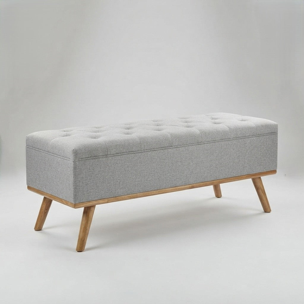 A rectangular upholstered storage bench with a tufted light gray fabric seat and natural wood legs, shown on a plain light gray studio background.