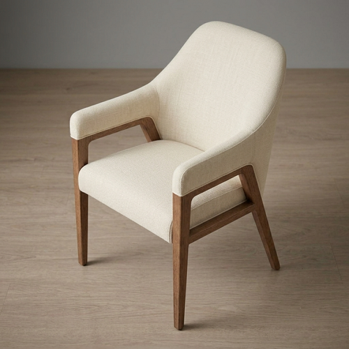A modern accent chair with cream-colored textured fabric upholstery and a medium brown wooden frame, shown on a light wood floor against a neutral gray wall.