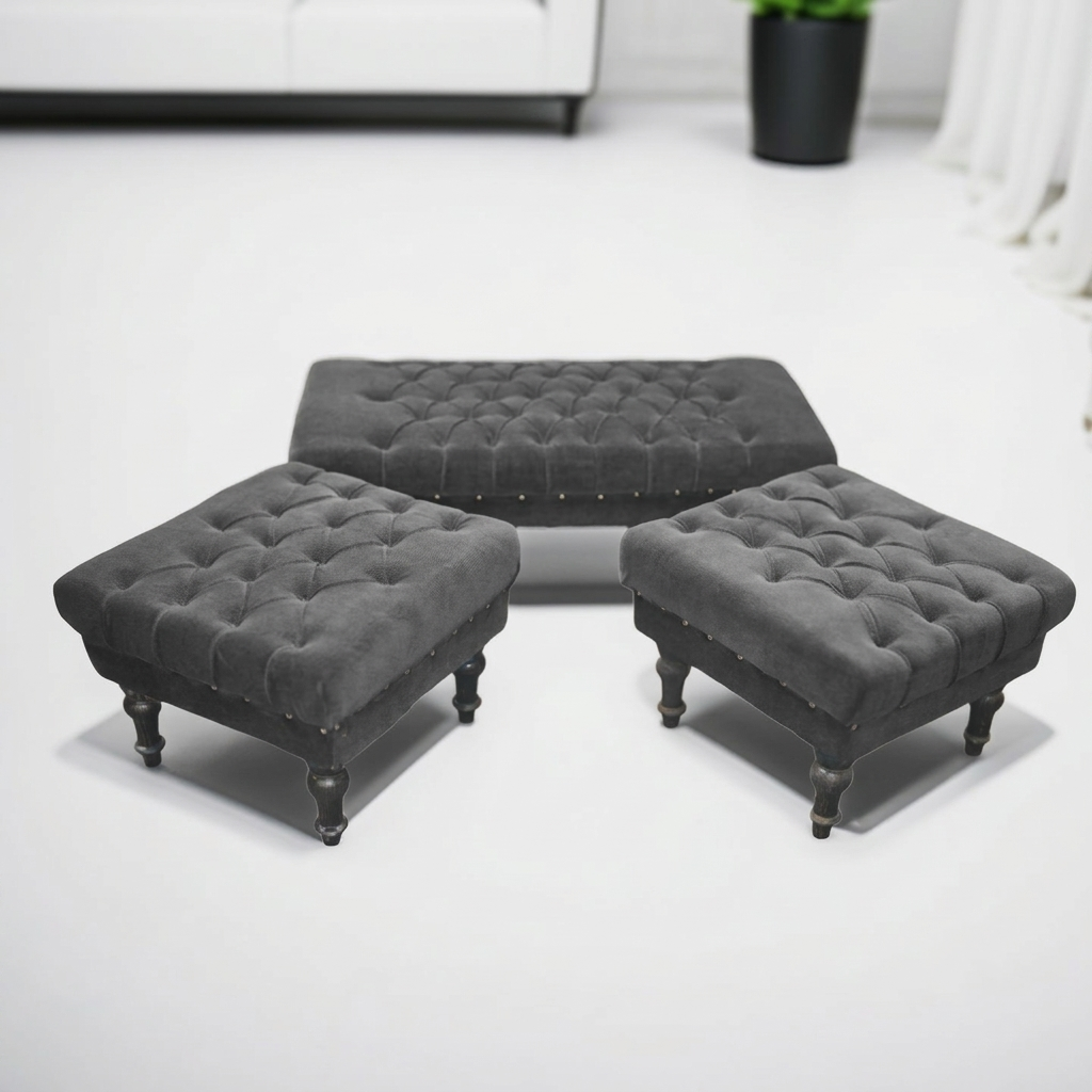 Three dark gray tufted ottomans with dark wooden legs arranged on a white floor in a bright room.