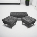Three dark gray tufted ottomans with dark wooden legs arranged on a white floor in a bright room.