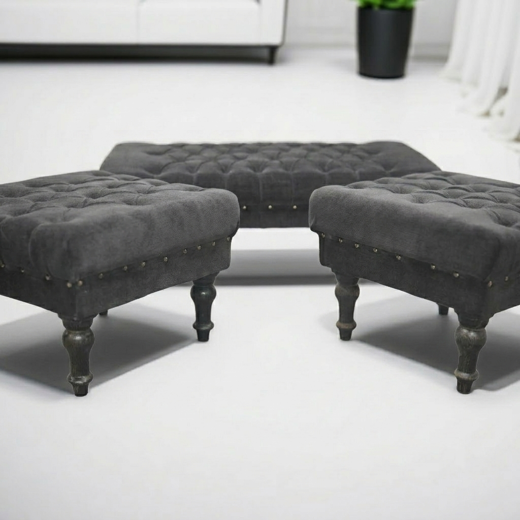 Three dark gray tufted velvet ottomans with turned legs and nailhead trim, arranged in a semi-circle on a light gray floor.