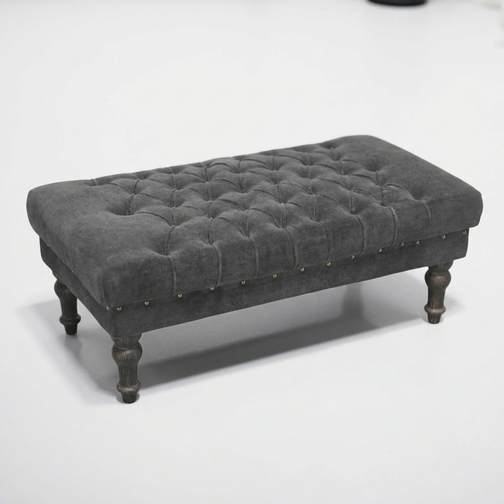 A rectangular tufted bench ottoman upholstered in dark gray velvet fabric, featuring decorative brass nailhead trim along the front edge and turned dark wood legs, shown on a plain white studio background.