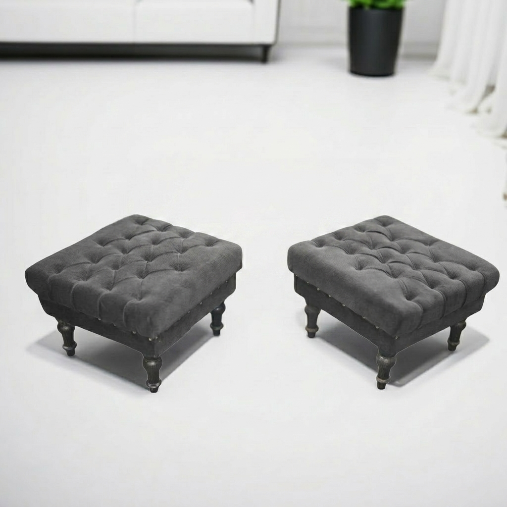 Two matching square tufted ottomans in dark gray velvet, each with turned dark legs and nailhead trim, shown on a clean white floor in a modern room setting.