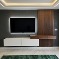 Modern wall-mounted TV setup in a living room, featuring a black flat-screen television with backlighting, a white floating media console, and a dark wood slatted accent wall section with a matching wood desk surface.