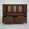 A dark brown wooden crib or bassinet with vertical slats and two pull-out storage drawers underneath, shown against a plain light gray studio background.