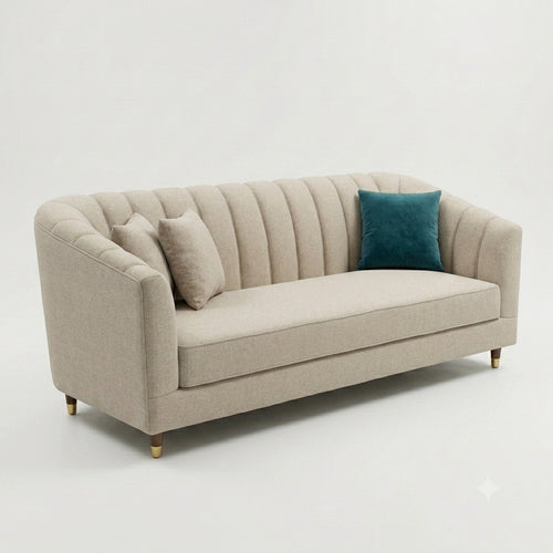 A modern three-seater sofa upholstered in light beige fabric with channel-tufted vertical detailing on the backrest and arms. The sofa is shown with two matching beige throw pillows and one teal accent pillow, supported by slim gold-toned legs, set against a clean white studio background.